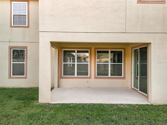 property entrance with a patio, a yard, and stucco siding