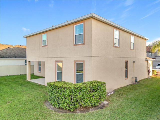 back of house featuring a patio, a lawn, fence, and stucco siding