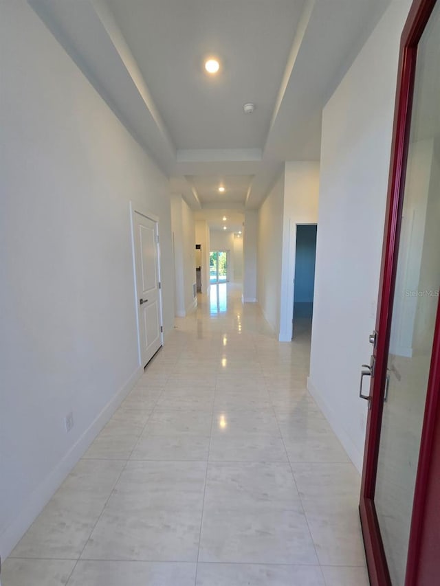 hallway featuring recessed lighting, a tray ceiling, baseboards, and light tile patterned flooring