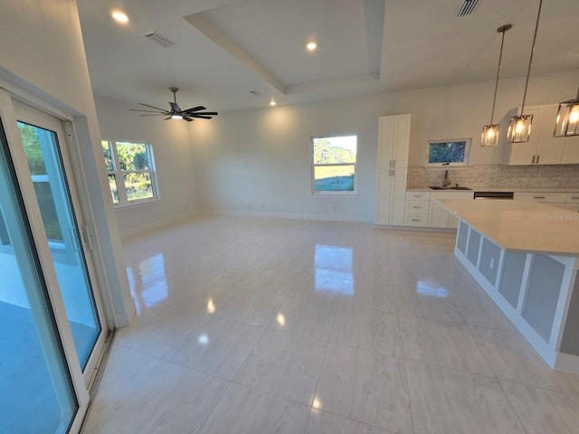 interior space featuring visible vents, baseboards, a tray ceiling, a ceiling fan, and a sink