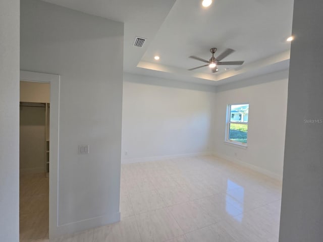 empty room featuring visible vents, a ceiling fan, a tray ceiling, recessed lighting, and baseboards