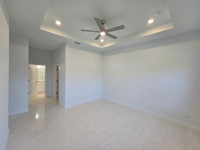 empty room featuring a tray ceiling, recessed lighting, baseboards, and visible vents