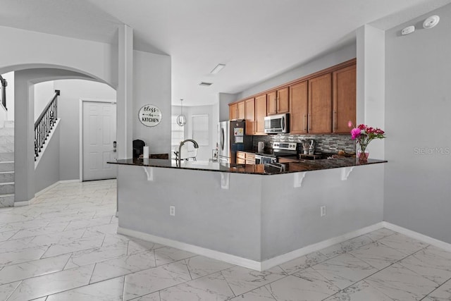 kitchen with marble finish floor, stainless steel appliances, a breakfast bar area, and brown cabinetry