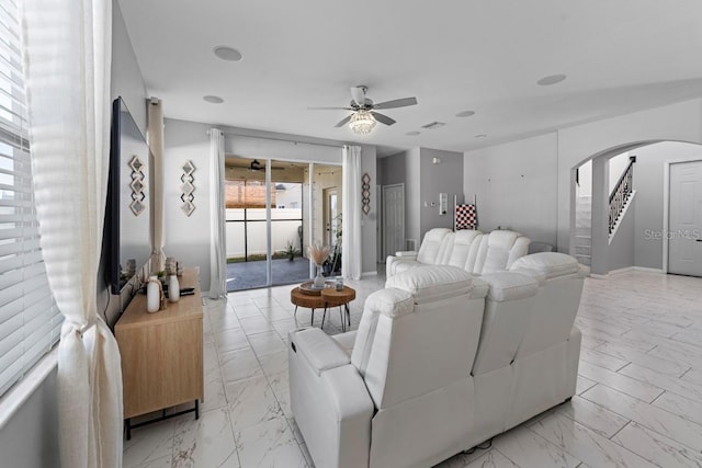 living area featuring a ceiling fan, arched walkways, marble finish floor, and stairs