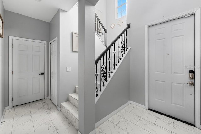 entryway featuring marble finish floor, stairs, and baseboards