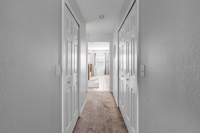 hallway with a textured wall, carpet flooring, and baseboards