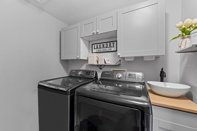 clothes washing area with cabinet space, a sink, washer and clothes dryer, and a textured ceiling