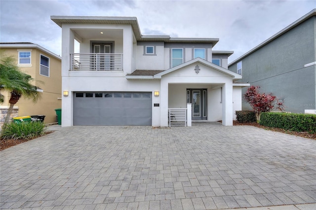 view of front facade with a balcony, a garage, decorative driveway, and stucco siding