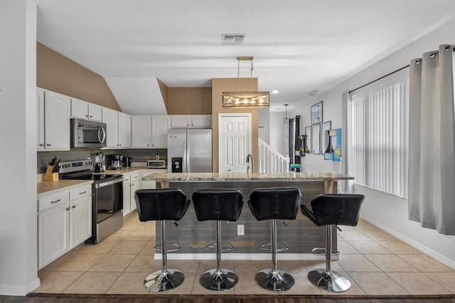 kitchen featuring light tile patterned floors, visible vents, a breakfast bar, stainless steel appliances, and white cabinets