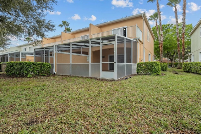 rear view of house featuring a lawn, glass enclosure, a balcony, and stucco siding