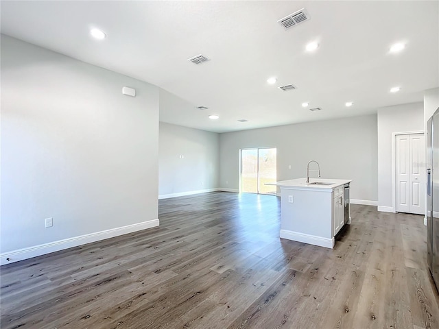 kitchen featuring an island with sink, a sink, visible vents, and light wood-style floors