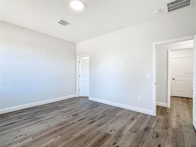 spare room featuring baseboards, visible vents, and wood finished floors