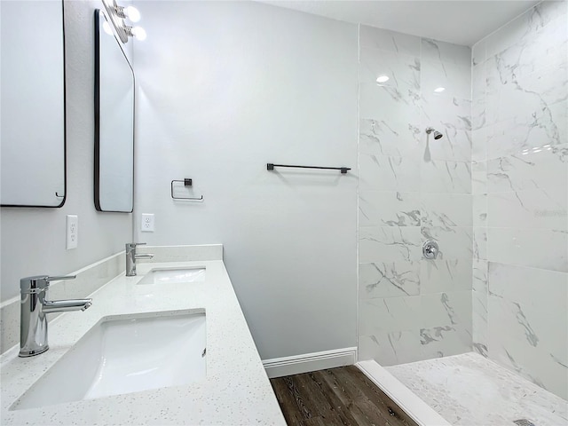 bathroom featuring double vanity, a tile shower, a sink, and wood finished floors