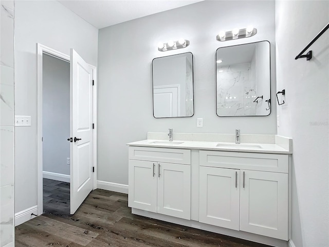 full bath featuring double vanity, wood finished floors, a sink, and baseboards