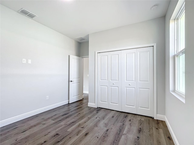 unfurnished bedroom with a closet, visible vents, baseboards, and wood finished floors