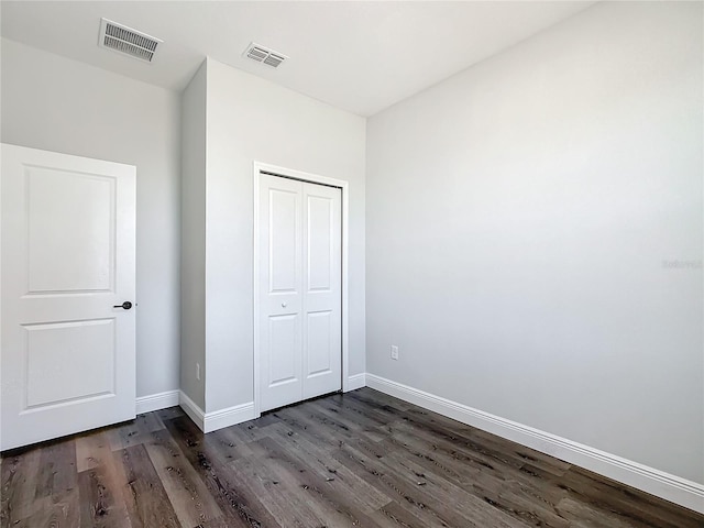 unfurnished bedroom with dark wood-style floors, baseboards, visible vents, and a closet