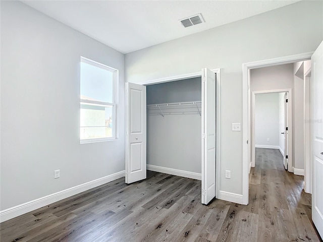 unfurnished bedroom with a closet, wood finished floors, visible vents, and baseboards