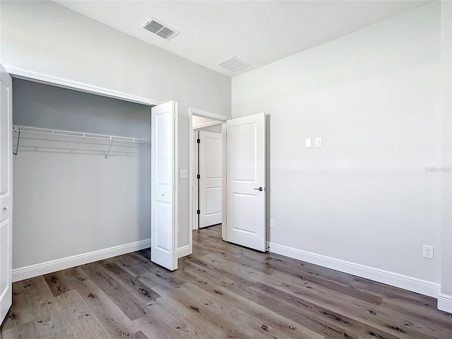 unfurnished bedroom with a closet, wood finished floors, visible vents, and baseboards