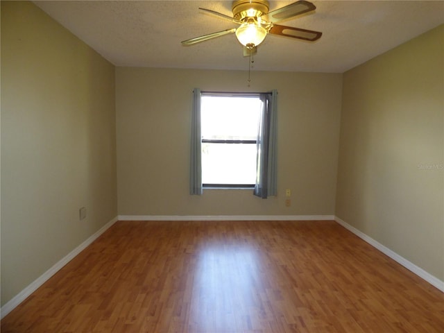 empty room with ceiling fan, a textured ceiling, baseboards, and wood finished floors