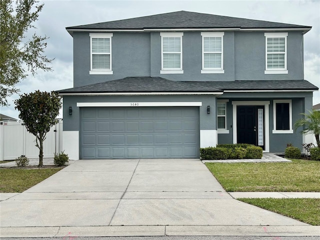 traditional-style house featuring fence, driveway, stucco siding, a front lawn, and a garage