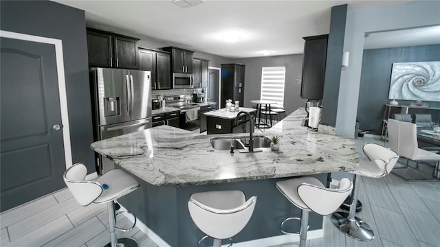 kitchen with light stone counters, a sink, appliances with stainless steel finishes, a kitchen breakfast bar, and backsplash