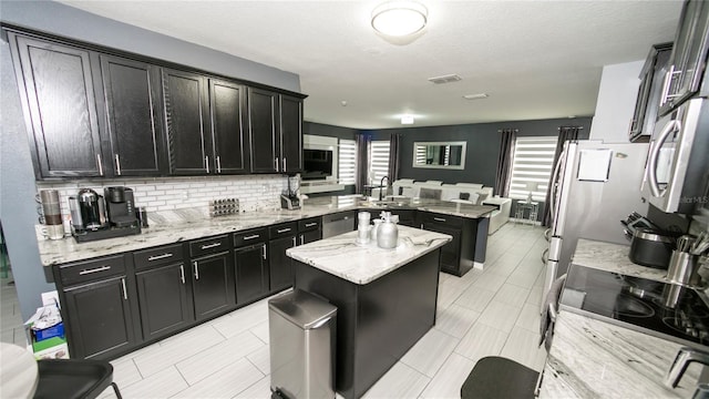 kitchen with dark cabinetry, visible vents, a peninsula, appliances with stainless steel finishes, and a center island