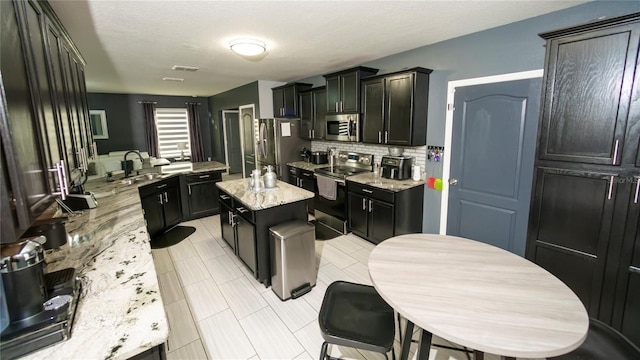 kitchen with light stone countertops, a kitchen island, a sink, decorative backsplash, and stainless steel appliances