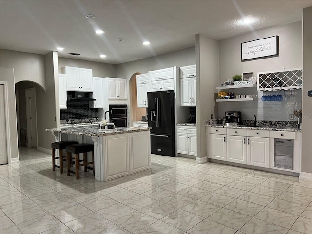 kitchen with arched walkways, a sink, black appliances, under cabinet range hood, and marble finish floor