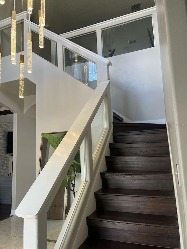 stairway with visible vents, marble finish floor, and a towering ceiling