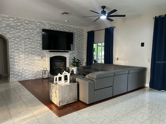 living area featuring visible vents, marble finish floor, a glass covered fireplace, arched walkways, and ceiling fan