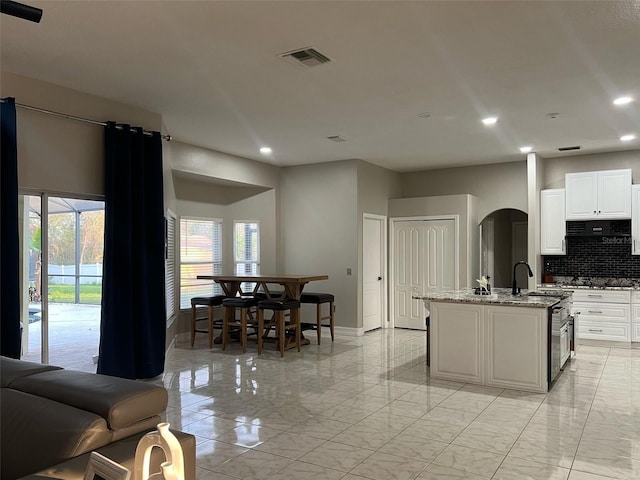 kitchen featuring light stone countertops, visible vents, arched walkways, decorative backsplash, and marble finish floor