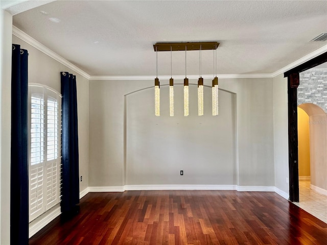 empty room featuring wood finished floors, visible vents, baseboards, arched walkways, and ornamental molding