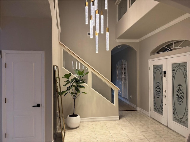 foyer entrance with crown molding, stairway, french doors, a high ceiling, and arched walkways