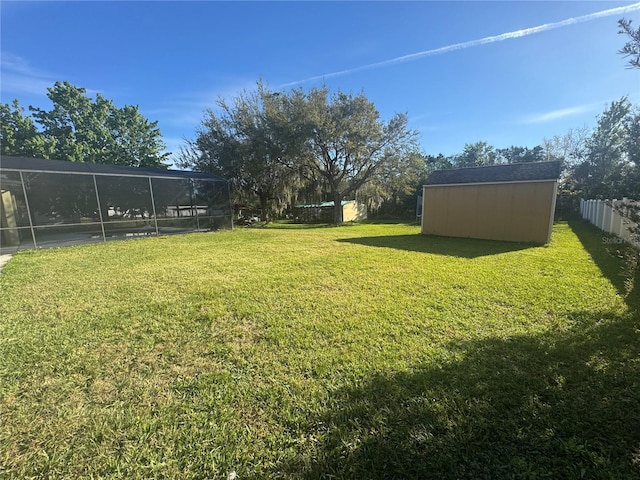 view of yard featuring a lanai, a storage unit, fence, and an outdoor structure