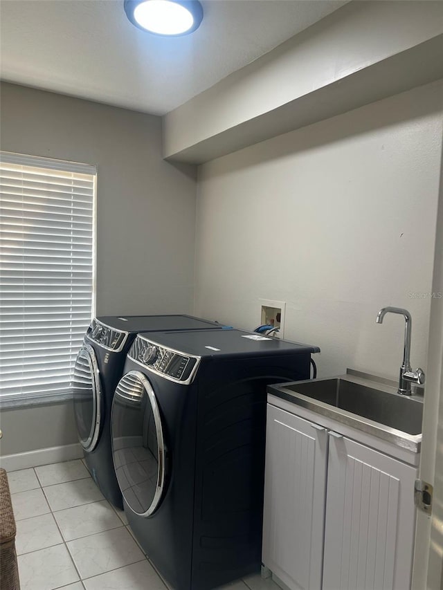 clothes washing area with baseboards, washing machine and dryer, light tile patterned flooring, cabinet space, and a sink