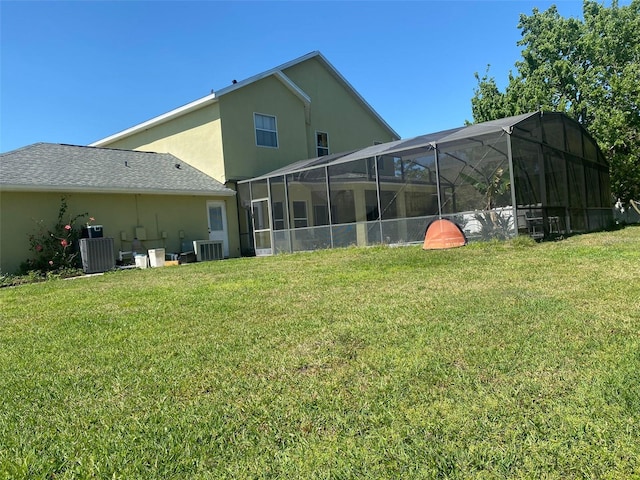 rear view of house featuring a lanai, cooling unit, a lawn, and stucco siding