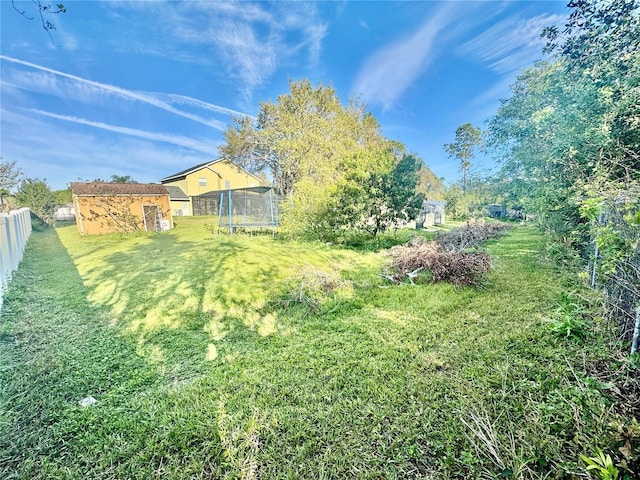 view of yard with fence, a trampoline, an outdoor structure, and a shed