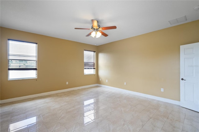 spare room with ceiling fan, visible vents, baseboards, and a wealth of natural light