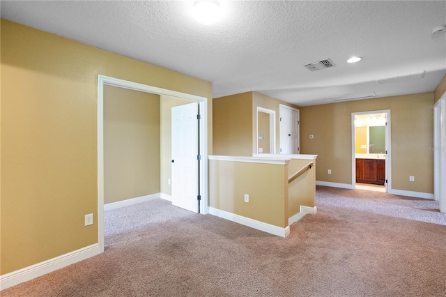 empty room featuring light carpet, baseboards, visible vents, a textured ceiling, and recessed lighting