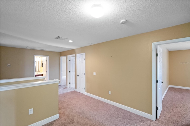 empty room featuring carpet floors, visible vents, a textured ceiling, and baseboards