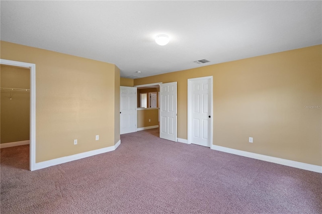 unfurnished bedroom with carpet floors, a walk in closet, a closet, visible vents, and baseboards