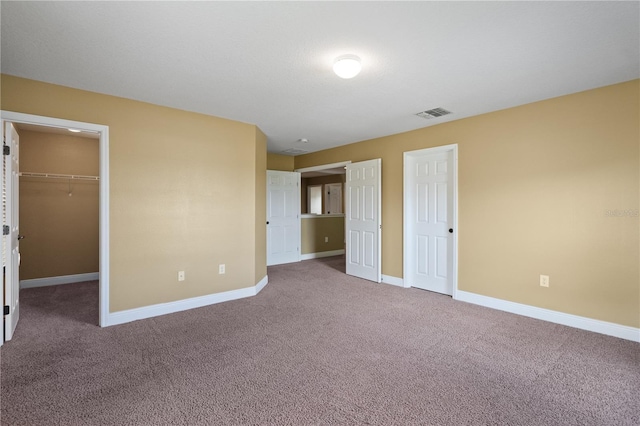 unfurnished bedroom featuring carpet floors, visible vents, baseboards, a closet, and a walk in closet