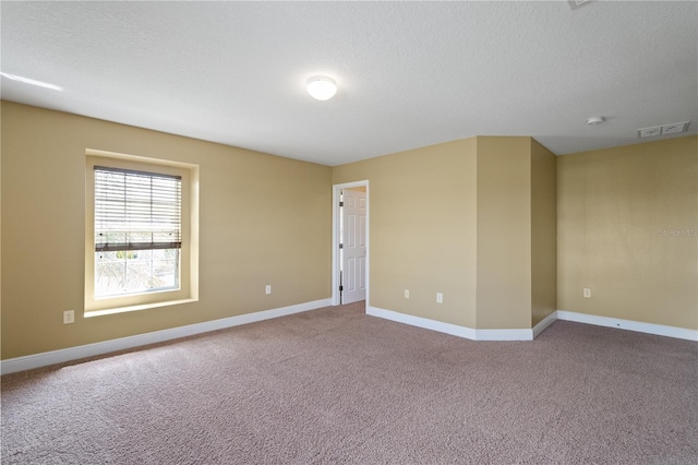 carpeted spare room with a textured ceiling, visible vents, and baseboards