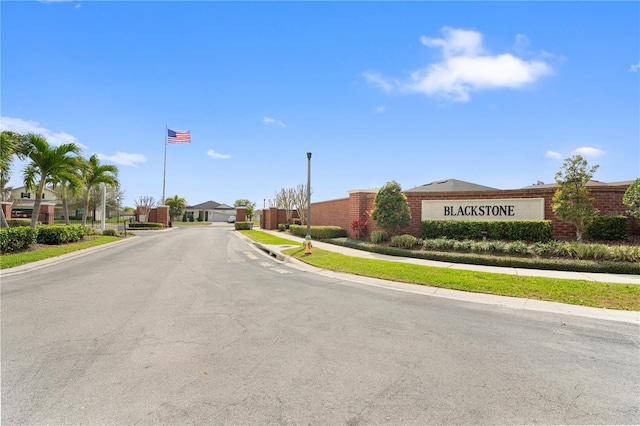 view of road featuring curbs, street lighting, a gated entry, and sidewalks