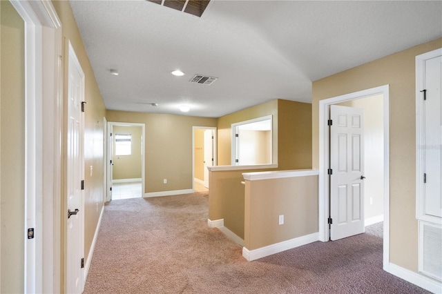 hallway featuring light carpet, baseboards, visible vents, and an upstairs landing