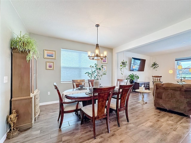 dining area with a notable chandelier, a textured ceiling, baseboards, and light wood-style floors