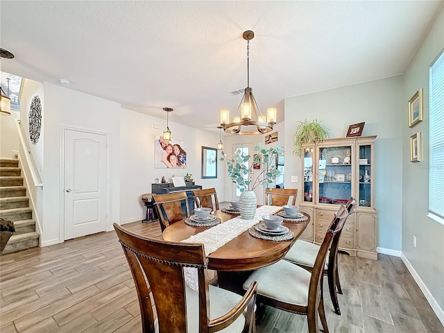 dining area with a notable chandelier, visible vents, light wood-type flooring, baseboards, and stairs