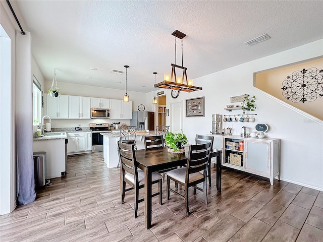 dining space featuring a textured ceiling, an inviting chandelier, visible vents, and wood tiled floor