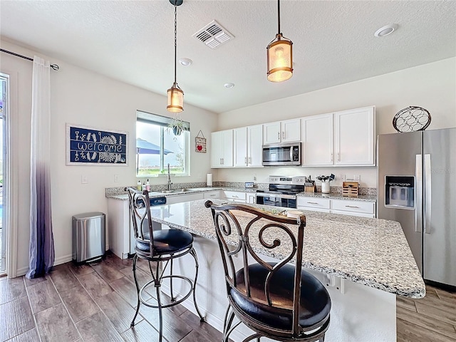 kitchen featuring light wood-style flooring, a breakfast bar, visible vents, white cabinetry, and appliances with stainless steel finishes