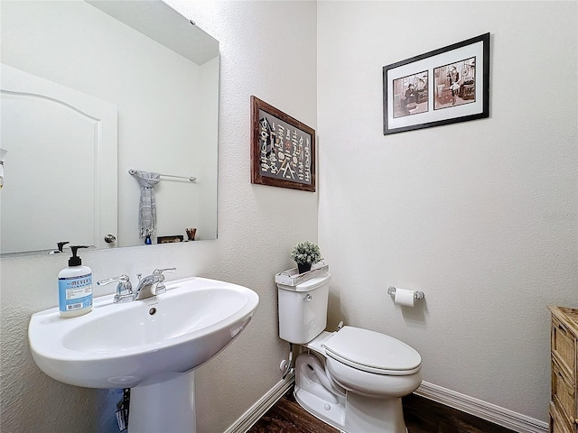 half bath with toilet, a sink, baseboards, and wood finished floors